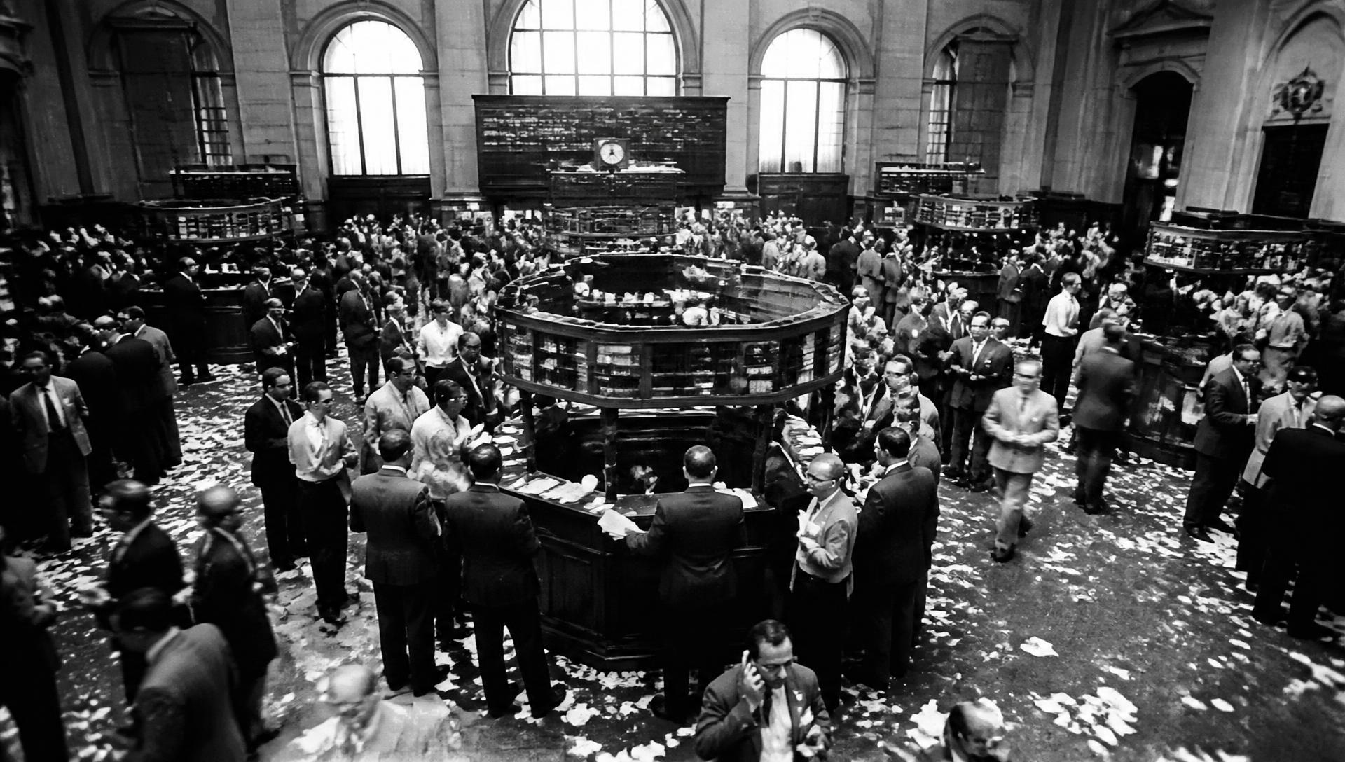 Archival photograph of traders crowded around posts on a mid-twentieth-century stock exchange floor